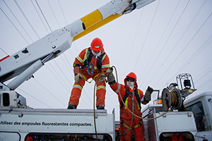 Deux préposés à l’entretien des lignes de transport d’électricité au travail à l’extérieur lors d’une journée froide d’hiver.